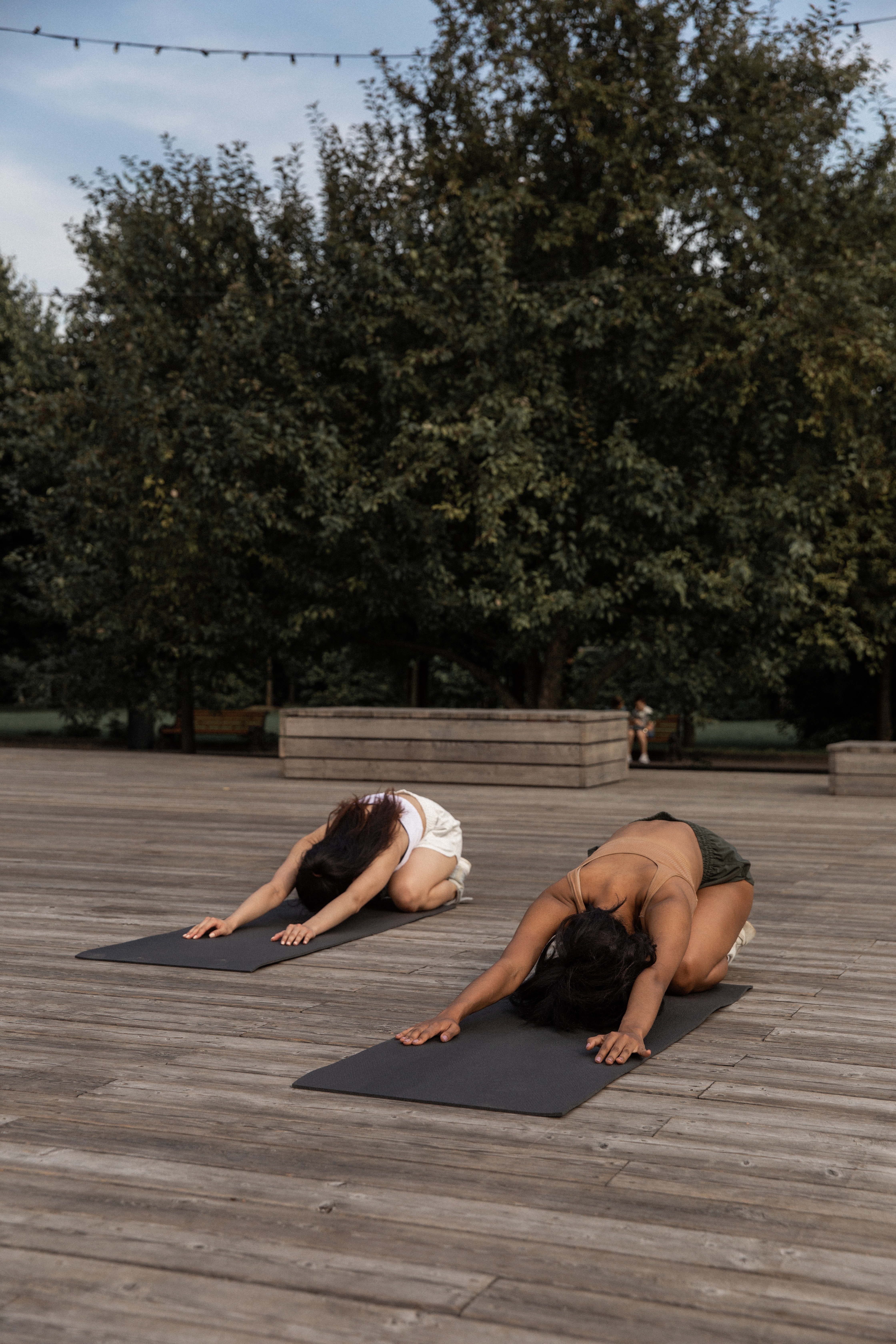 Two ladies doing child yoga pose outdoors.
